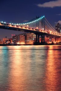 Manhattan Bridge over East River at night in New York City Manhattan with lights and reflections.